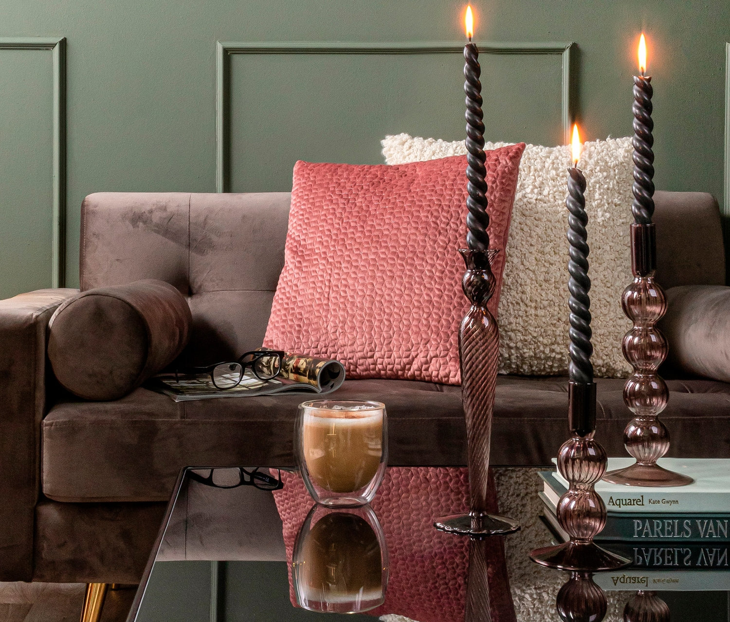 Drei brennende schwarze Kerzen in braunen Kerzenständern auf einem Tisch vor einem Sofa.