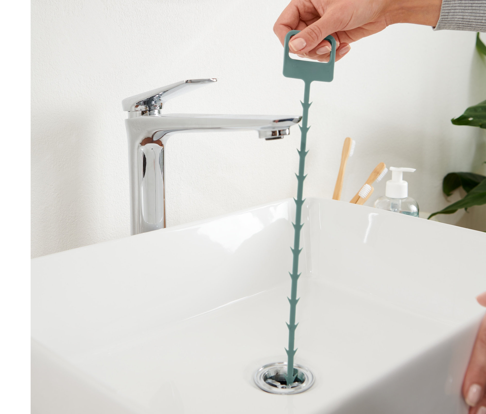 Eine Hand führt einen Abflussreiniger in den Abfluss eines Waschbeckens ein.