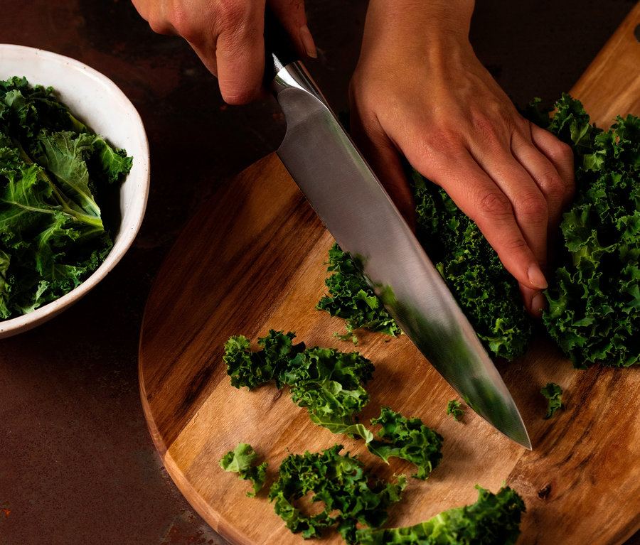 Frau schneidet Grünkohl mit einem WILFA Kochmesser EGO Sandvik »ES20CK« auf einem Holzbrett. In einer Schüssel befindet sich weiterer Grünkohl.