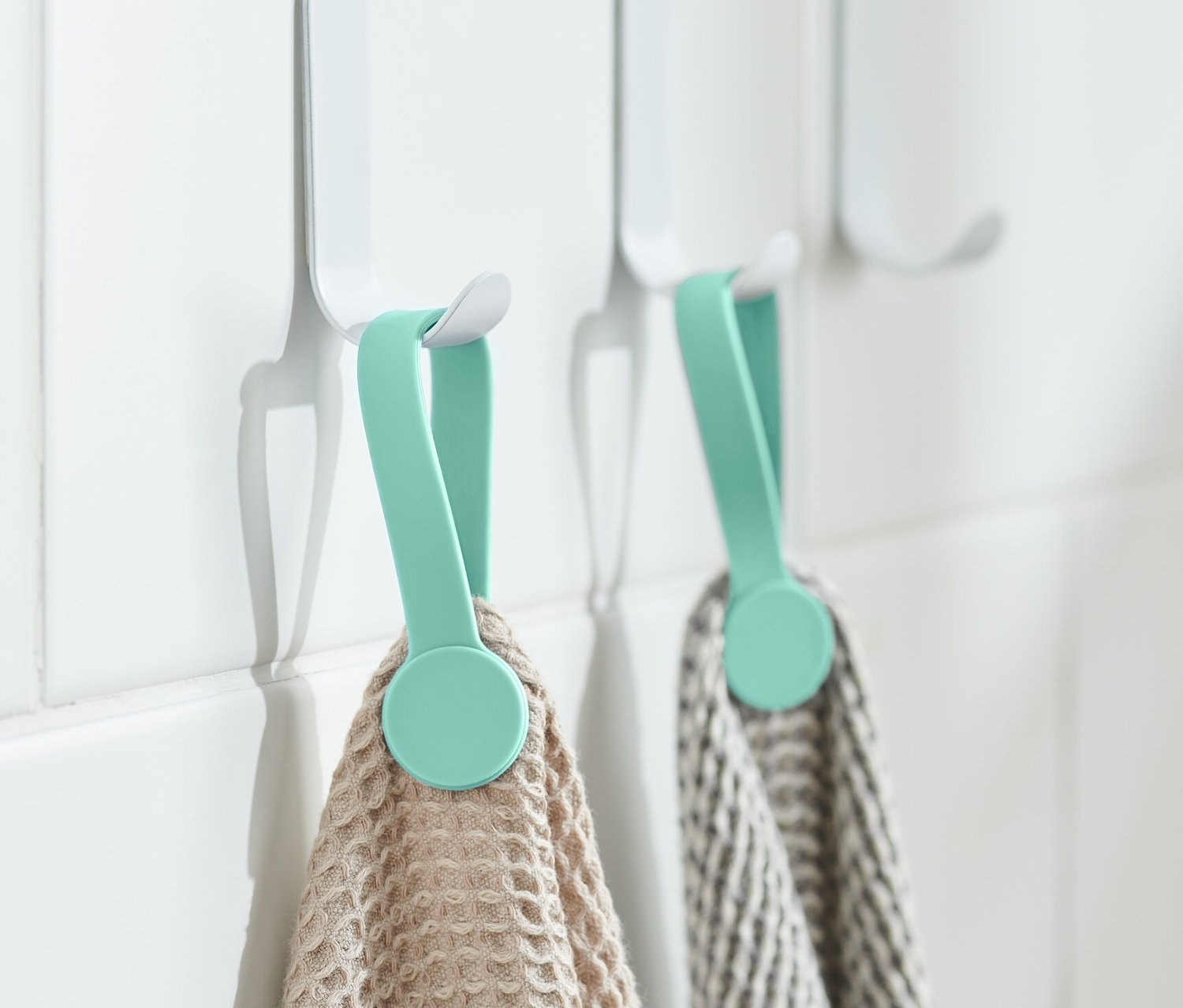 Zwei Magnet-Clips halten Handtücher an weißen Haken an der Wand.