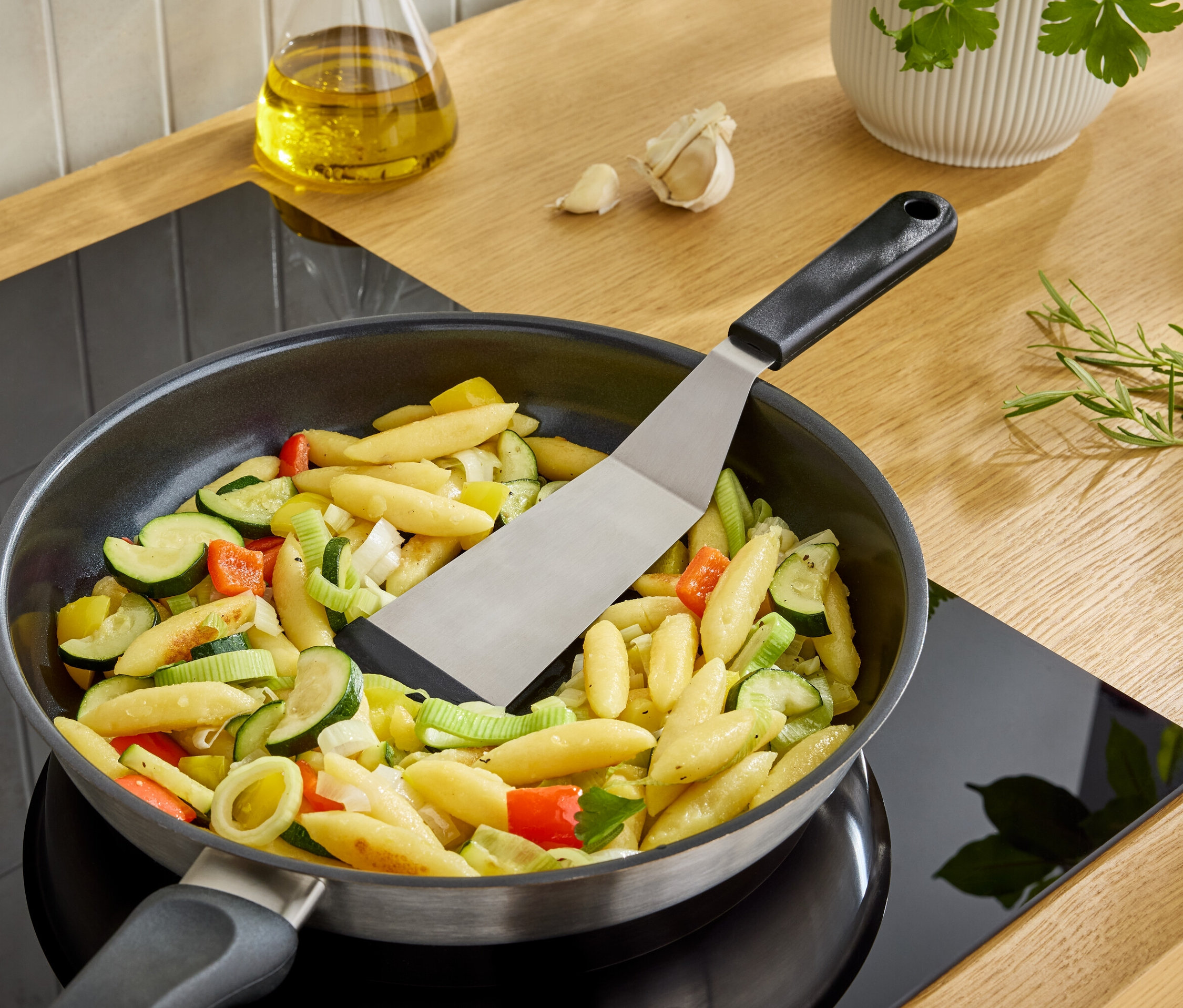 Ein Pfannenwender wendet Schupfnudeln mit Gemüse in einer Pfanne auf einem Herd.