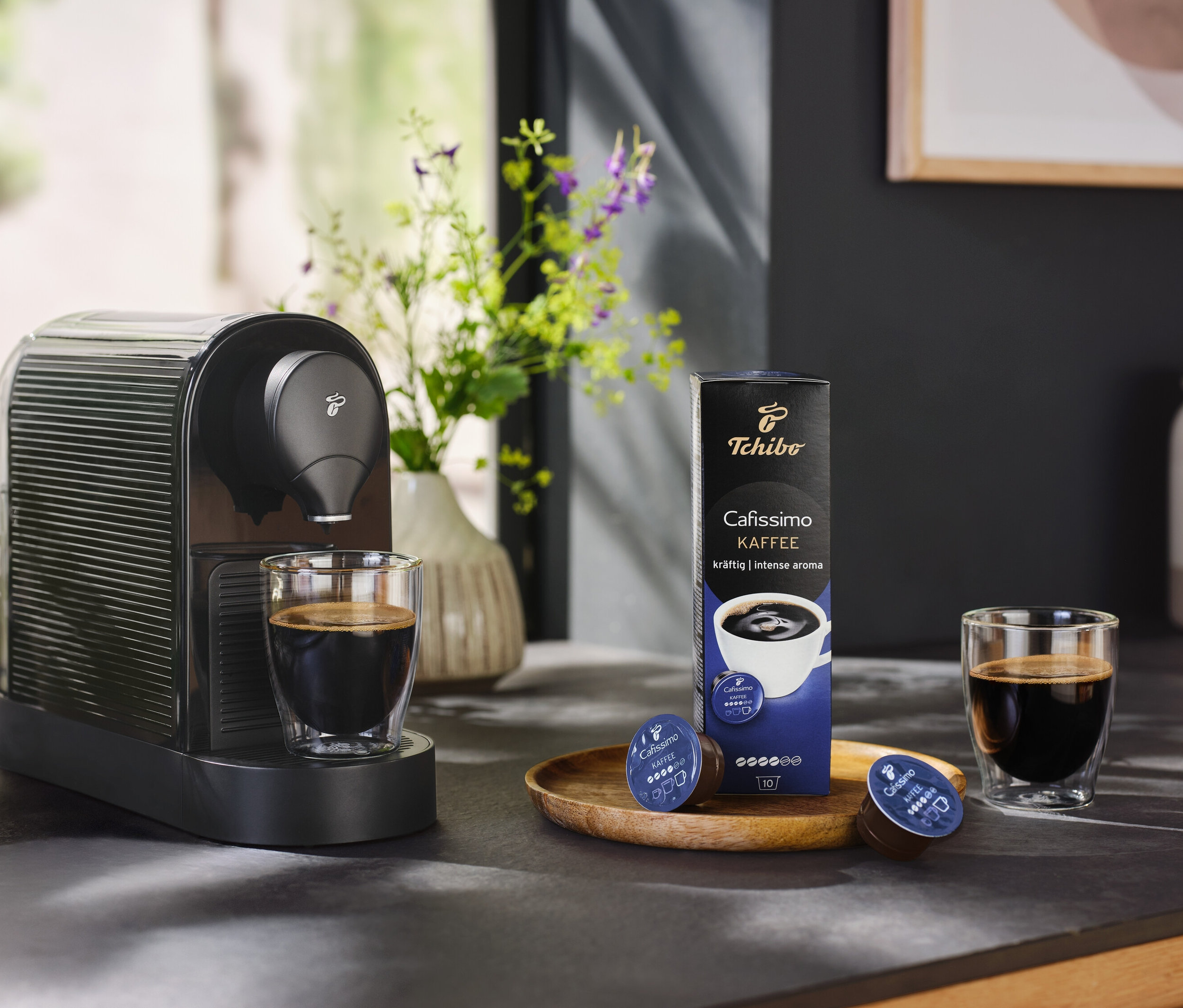 Schwarze Cafissimo pure+ mit einer Tasse Kaffee und einer Packung Kaffeekapseln.