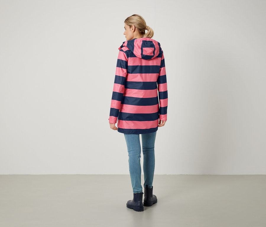 Frau von hinten trägt einen rosa-blau gestreiften Mantel, Jeans und Gummistiefel.