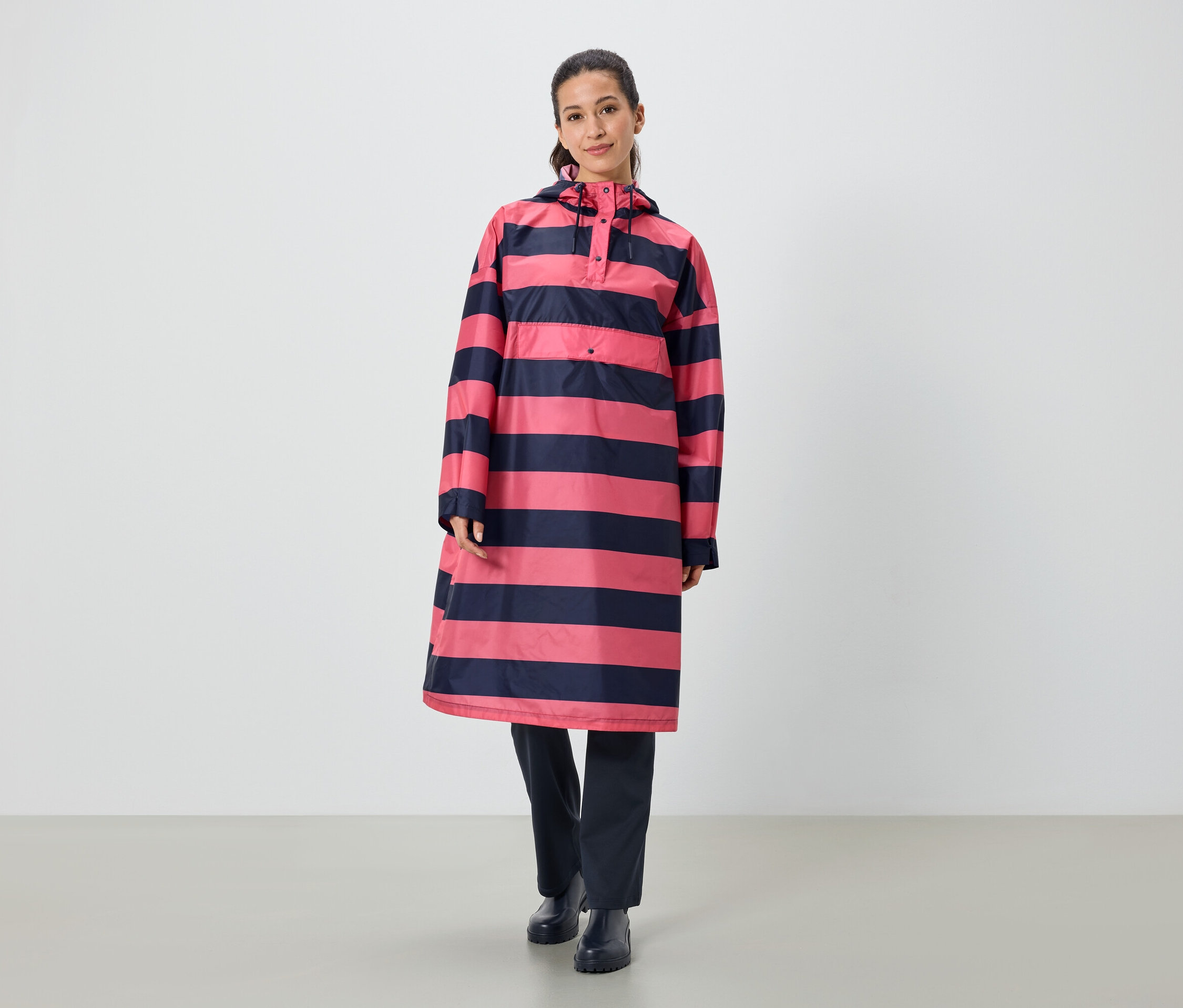 Eine Frau steht und trägt ein gestreiftes, rosa-marineblaues Regenponcho.