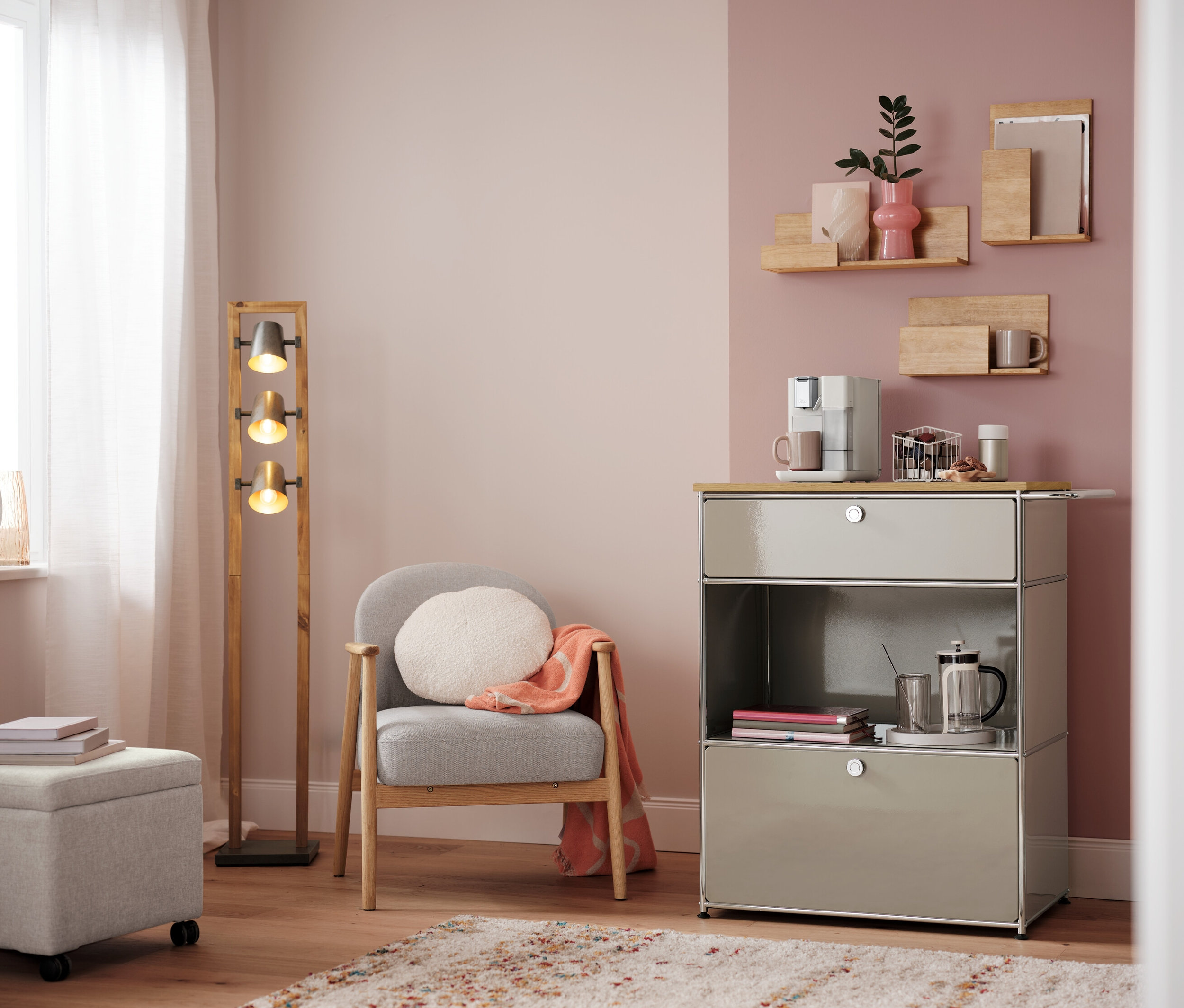 Wohnzimmer mit Sessel, Lampe und Kommode mit Kaffeemaschine. Auf der Kommode steht ein Kapselkorb, weiß.