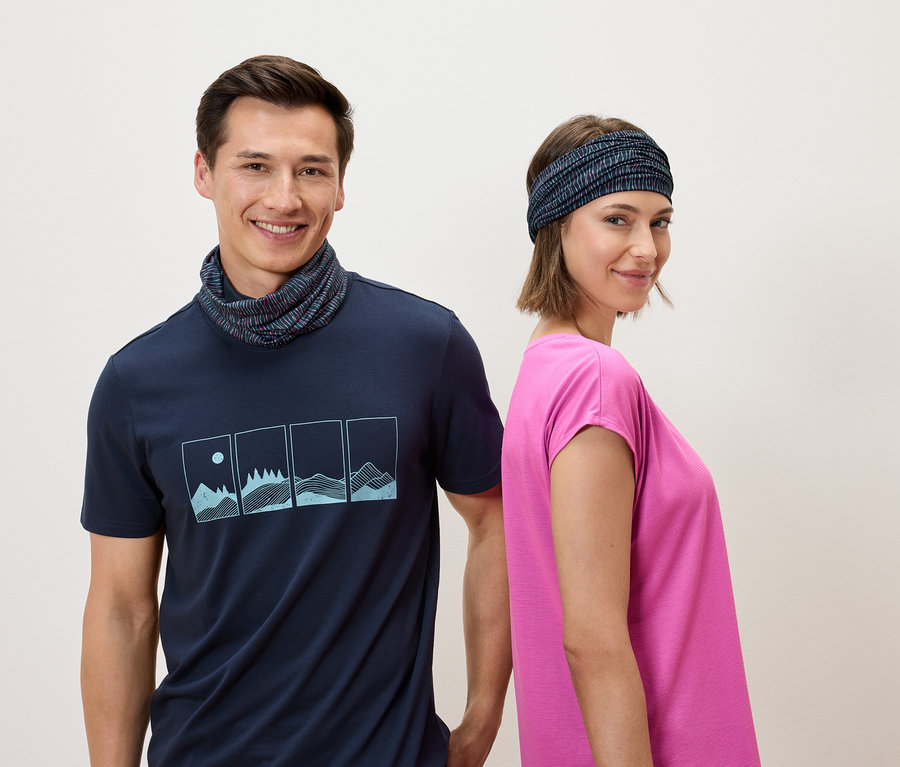 Ein Mann mit einem marineblauen T-Shirt und einem Halswärmer und eine Frau mit einem Stirnband und einem rosafarbenen T-Shirt stehen Rücken an Rücken vor einem weißen Hintergrund.