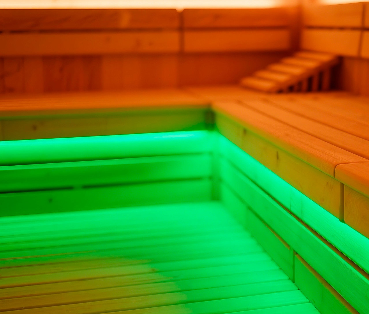 Innenansicht einer Sauna mit Holzbänken und grüner LED-Beleuchtung.
