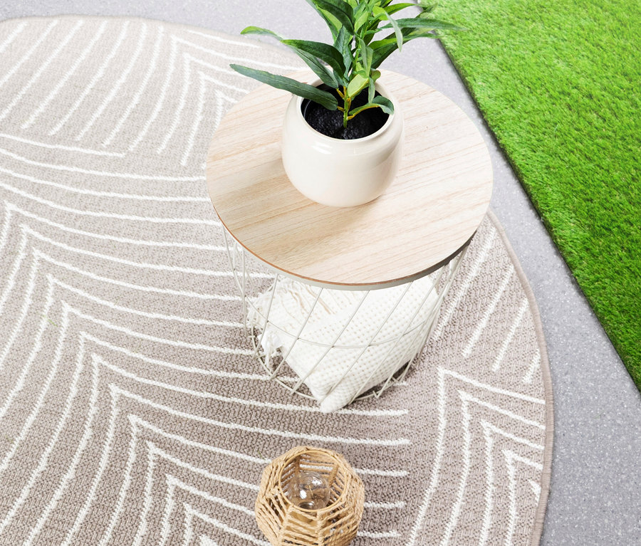 Draufsicht auf einen beigen Teppich mit weißem Zickzackmuster, einen runden Beistelltisch mit einer Topfpflanze und einen kleinen Weidenkorb.