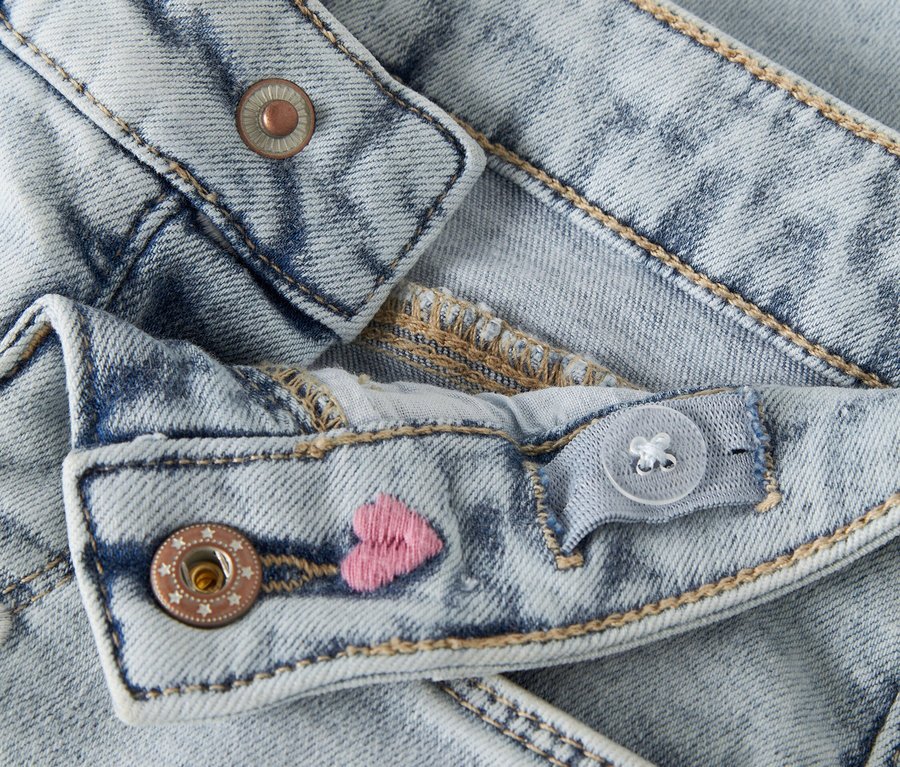 Detailaufnahme von hellblauen Jeans mit verstellbarem Bund, Knopfverschluss und gestickten rosa Herzen.