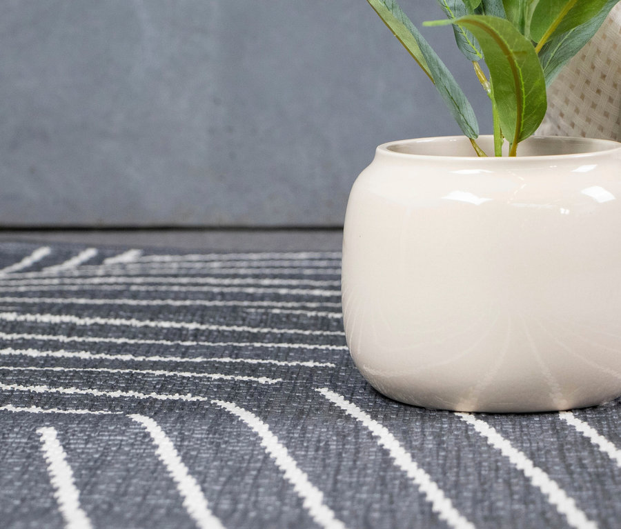 Nahaufnahme eines grauen Teppichs mit weißen Streifen und einer weißen Vase mit grünen Pflanzen.
