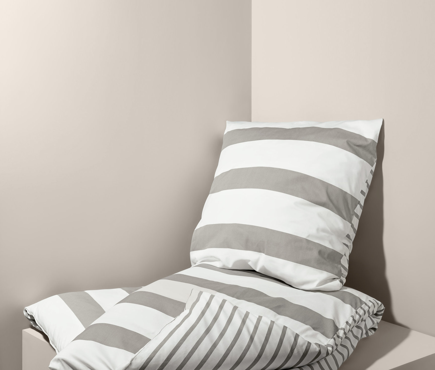 Gefaltete Perkal-Bettwäsche mit grauen Streifen, Normalgröße und Doppelgröße, liegt übereinander in einer Ecke.