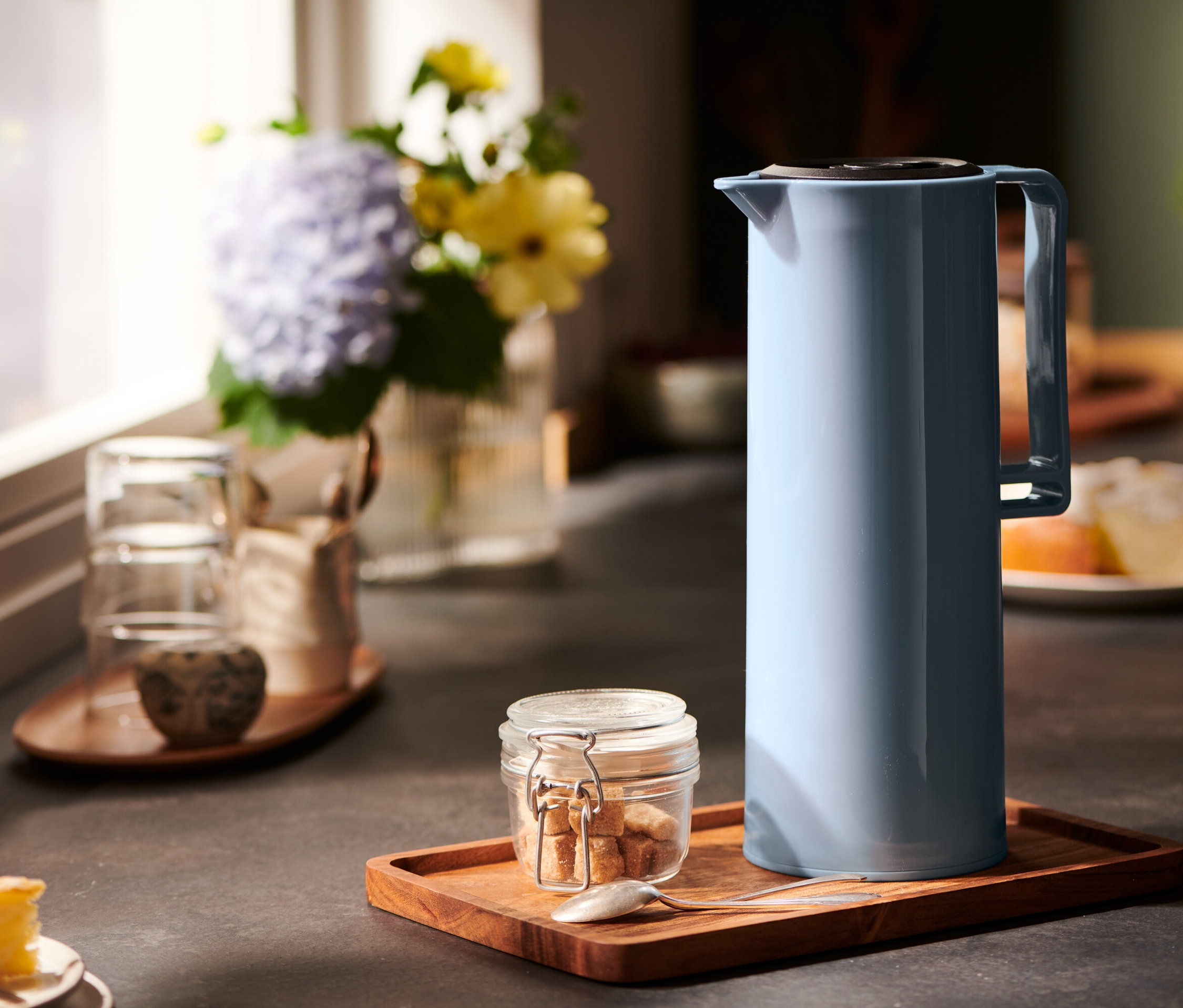 Eine blaue Isolierkanne steht auf einem Holztablett mit Zucker und einem Löffel.