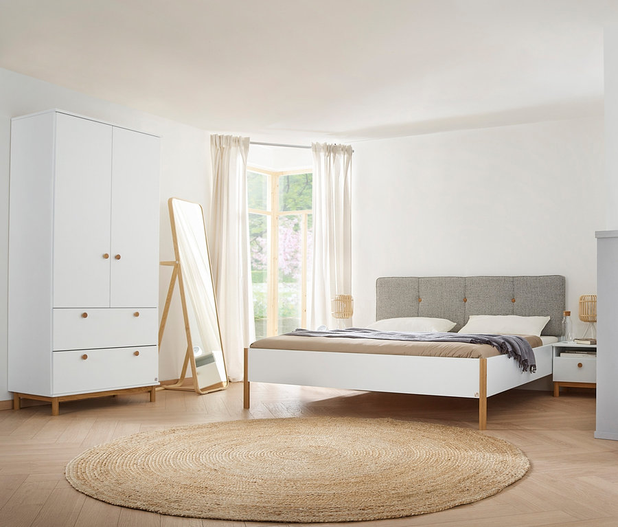 Schlafzimmer mit weißen Freyja-Möbeln: Drehtürenschrank, Kommode, 2 Nachttische. Im Vordergrund ein runder Teppich.