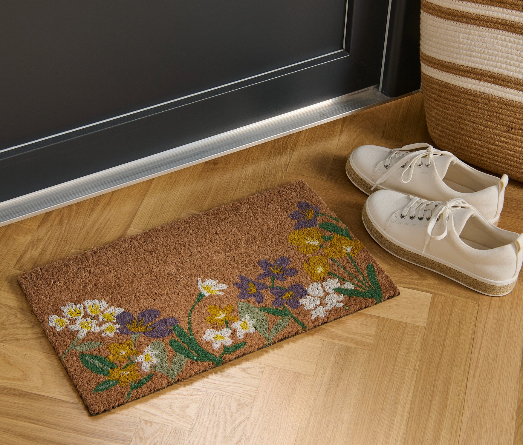 Eine Kokos-Fußmatte mit Blumenmuster liegt vor einer Tür.