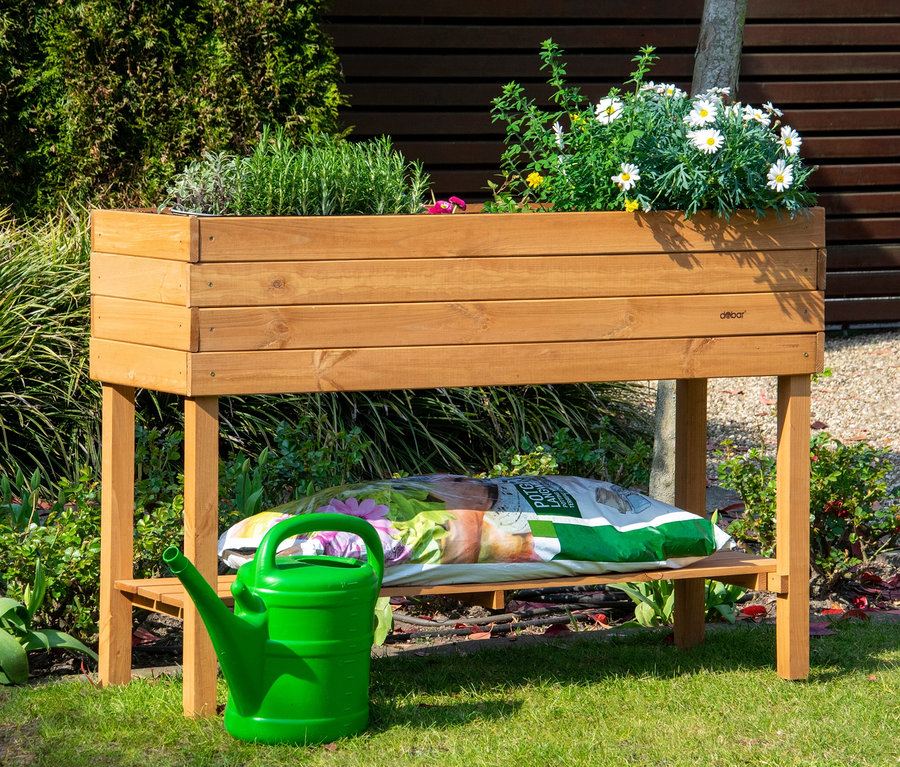 Ein Hochbeet, ca. 117 x 80 x 40 cm, befüllt mit Pflanzen, darunter ein Sack Erde und eine grüne Gießkanne.