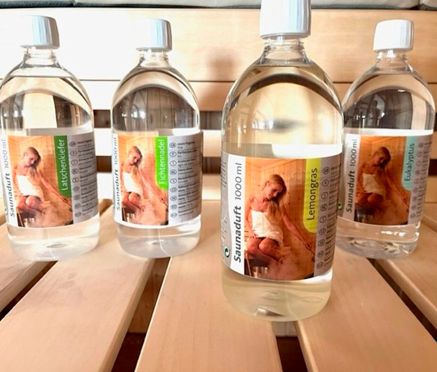 Vier Flaschen Karibu Sauna-Aufgusskonzentrat, 4x 1.000 ml, mit verschiedenen Düften stehen auf einer Holzfläche.