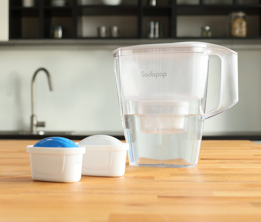 Auf einer Holzplatte stehen ein Sodapop Wasserfilter »Selina« und zwei Kartuschen.