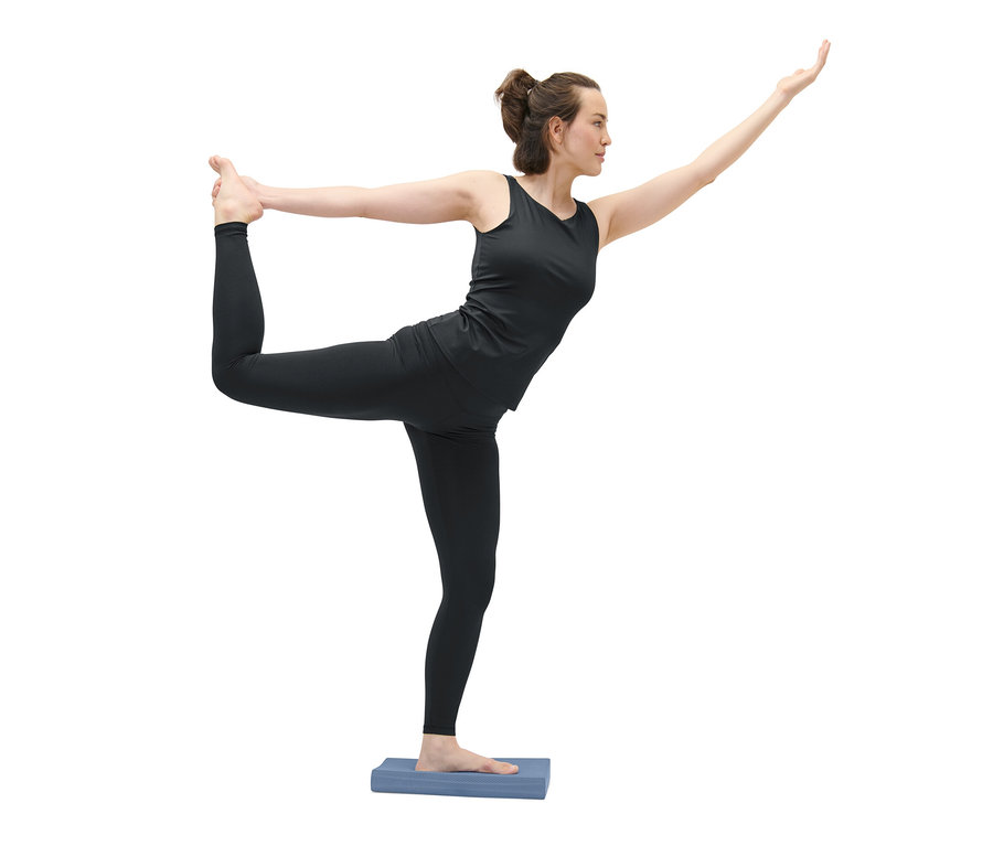 Frau in schwarzer Sportbekleidung steht auf einem Balance Pad in Tänzerpose.