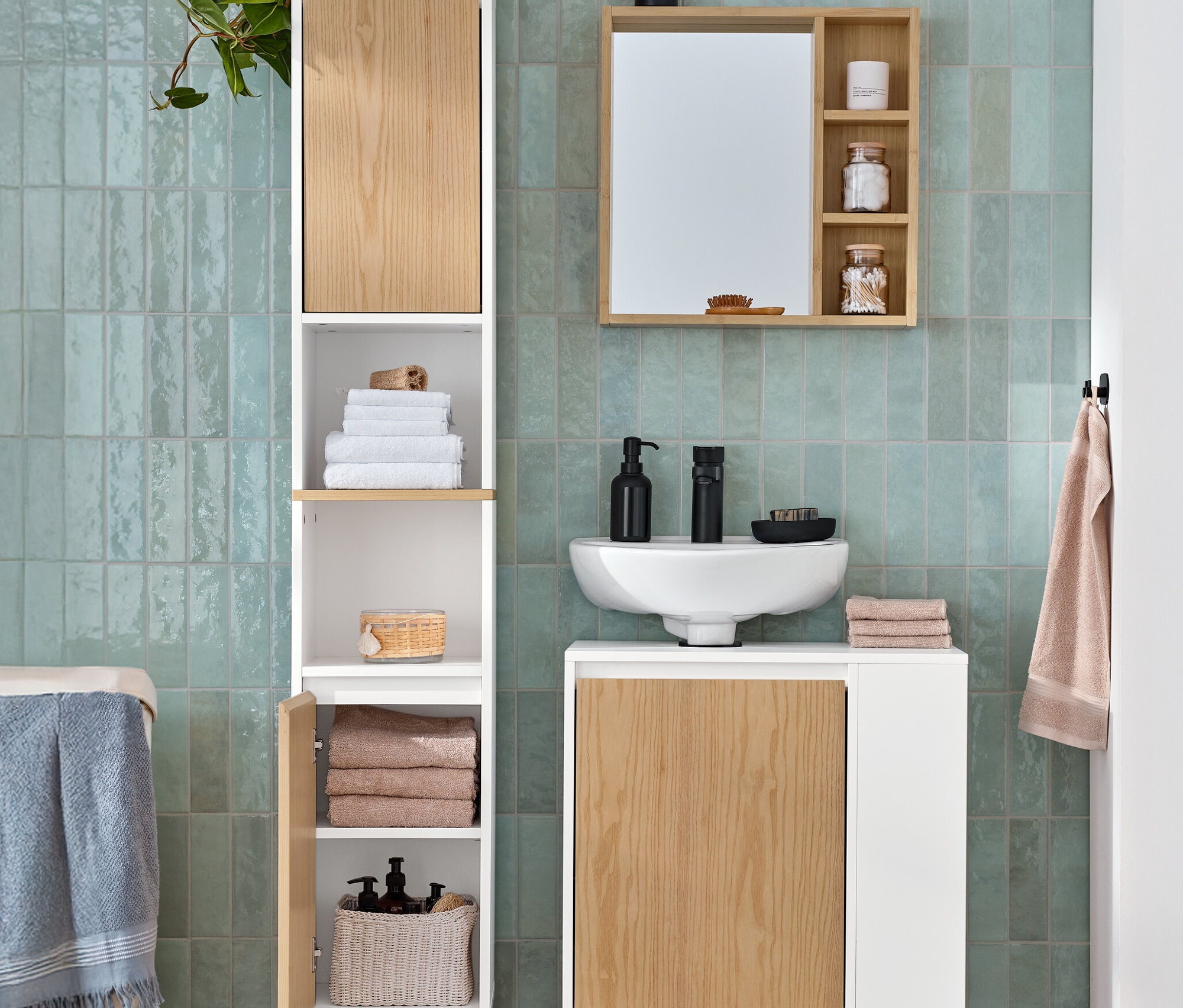 Ein Badezimmer zeigt einen Bad-Hochschrank mit offenem Fach und 2 Türen, einen Waschbeckenunterschrank mit Tür und seitlichem Fach und einen Spiegel mit Ablageflächen.