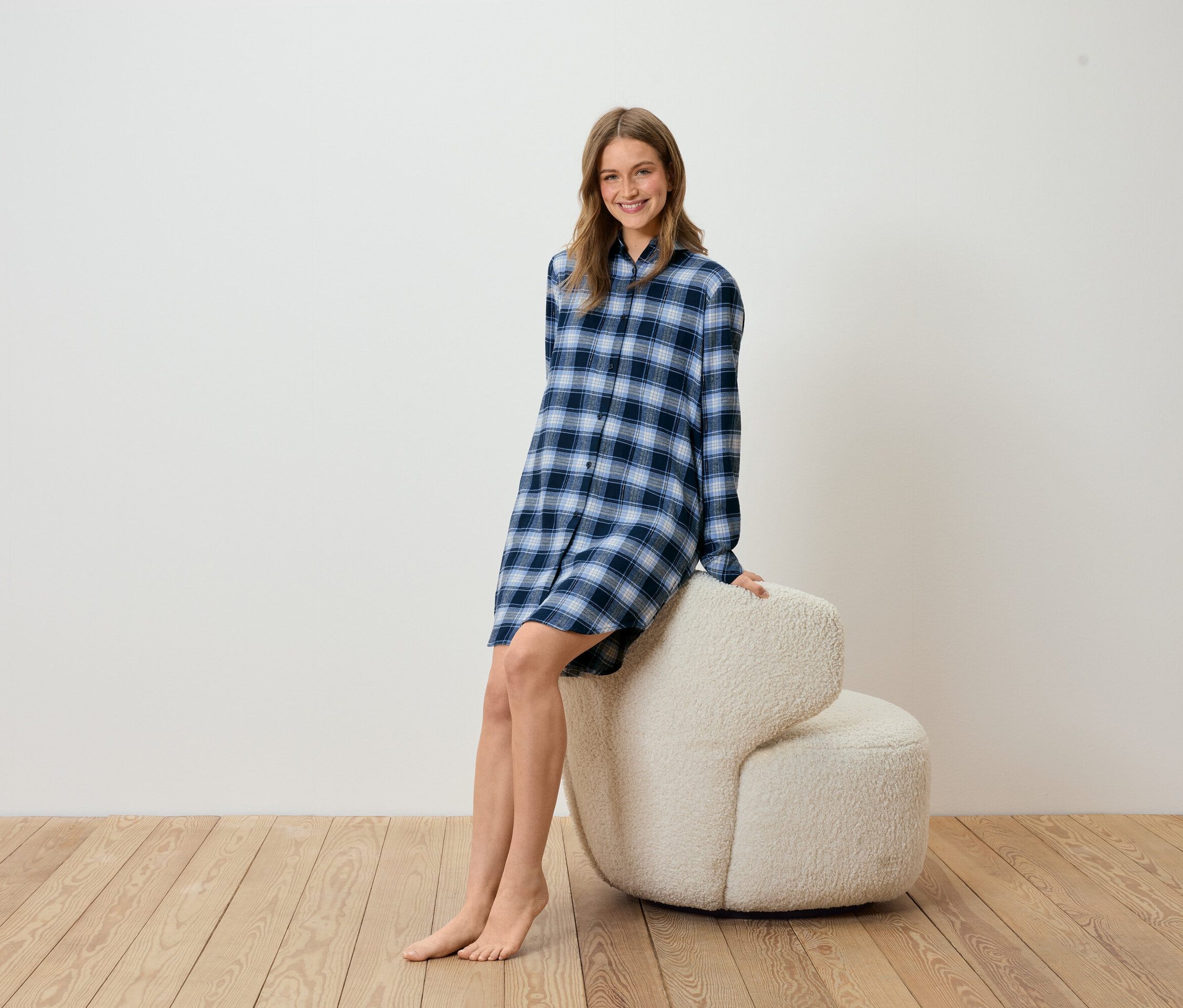 Frau sitzt auf beigem Sessel, trägt ein blau kariertes Nachthemd.