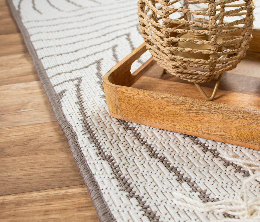 Nahaufnahme einer Korblampe auf einem Holztablett, das auf einem weißen Teppich mit geometrischem Muster auf einem Holzboden steht.