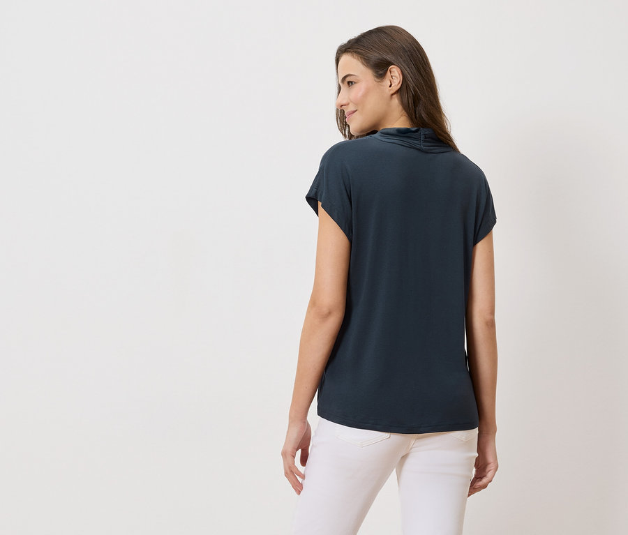 Rückansicht einer Frau mit langen braunen Haaren, die ein marineblaues Oberteil und weiße Jeans trägt.