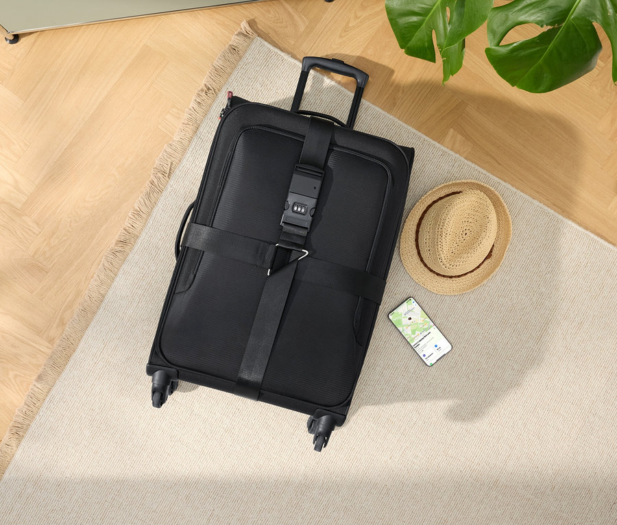 Schwarzer Rollkoffer mit Hut und Smartphone auf einem beigen Teppich.