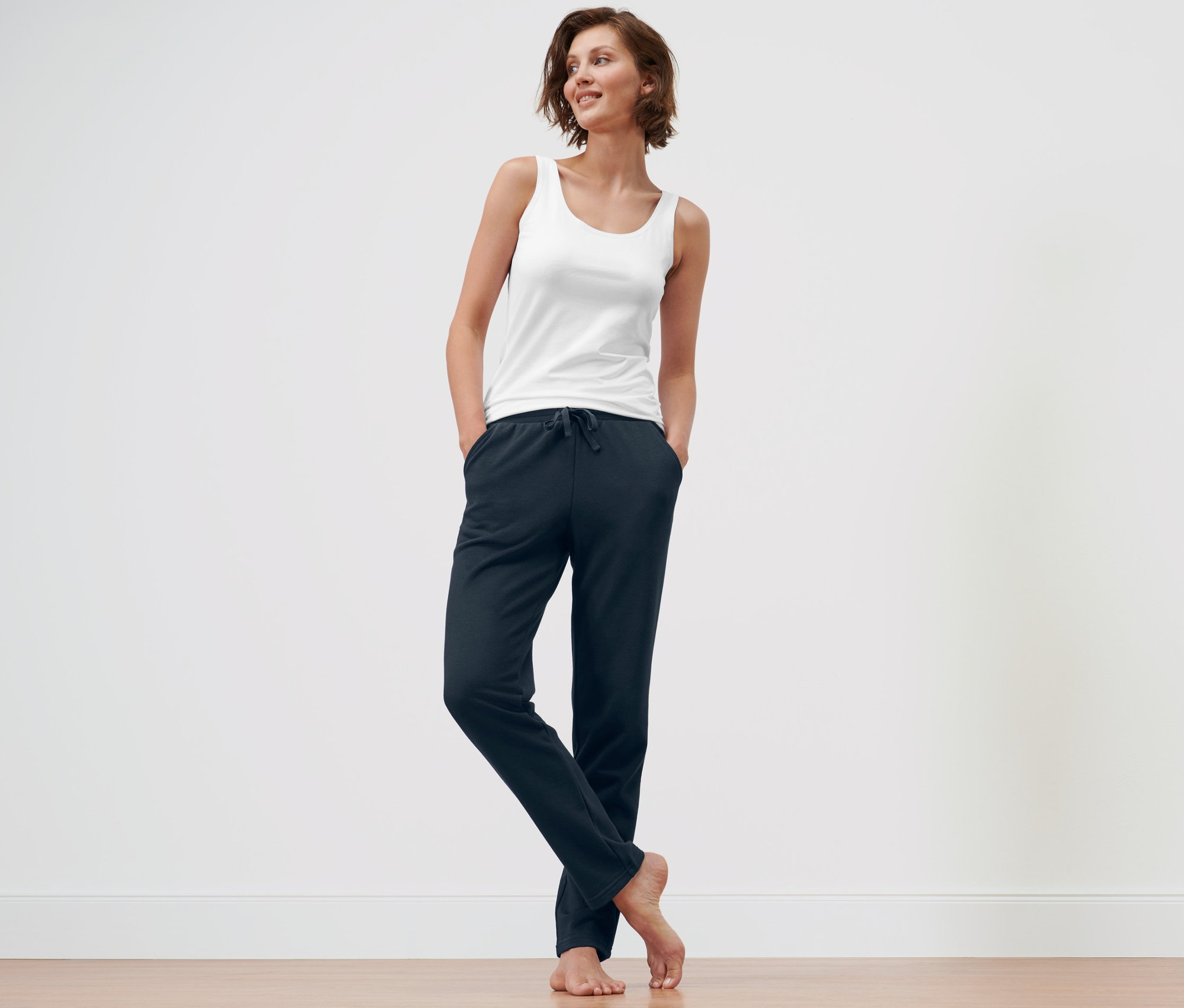 Frau steht mit Händen in den Taschen einer dunkelblauen Loungewear-Hose und einer blauen Loungehose.