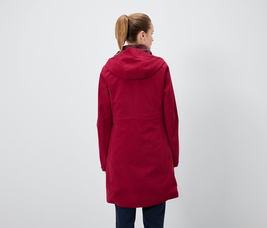 Rückansicht einer Frau mit Pferdeschwanz, die eine rote Kapuzenjacke und dunkelblaue Hosen trägt.