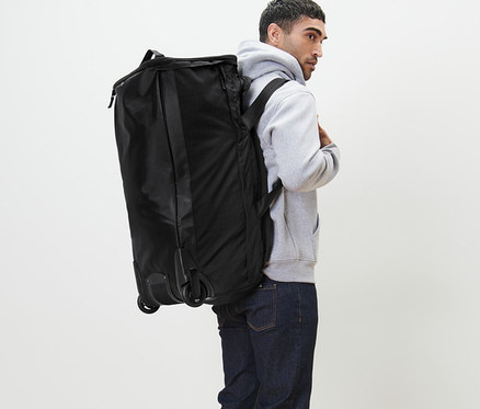 Mann trägt eine schwarze Rollentasche mit Rucksackfunktion.