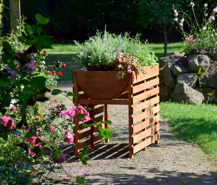 Ein braunes Hochbeet, XL, doppelt, mit Pflanzen steht im Garten.