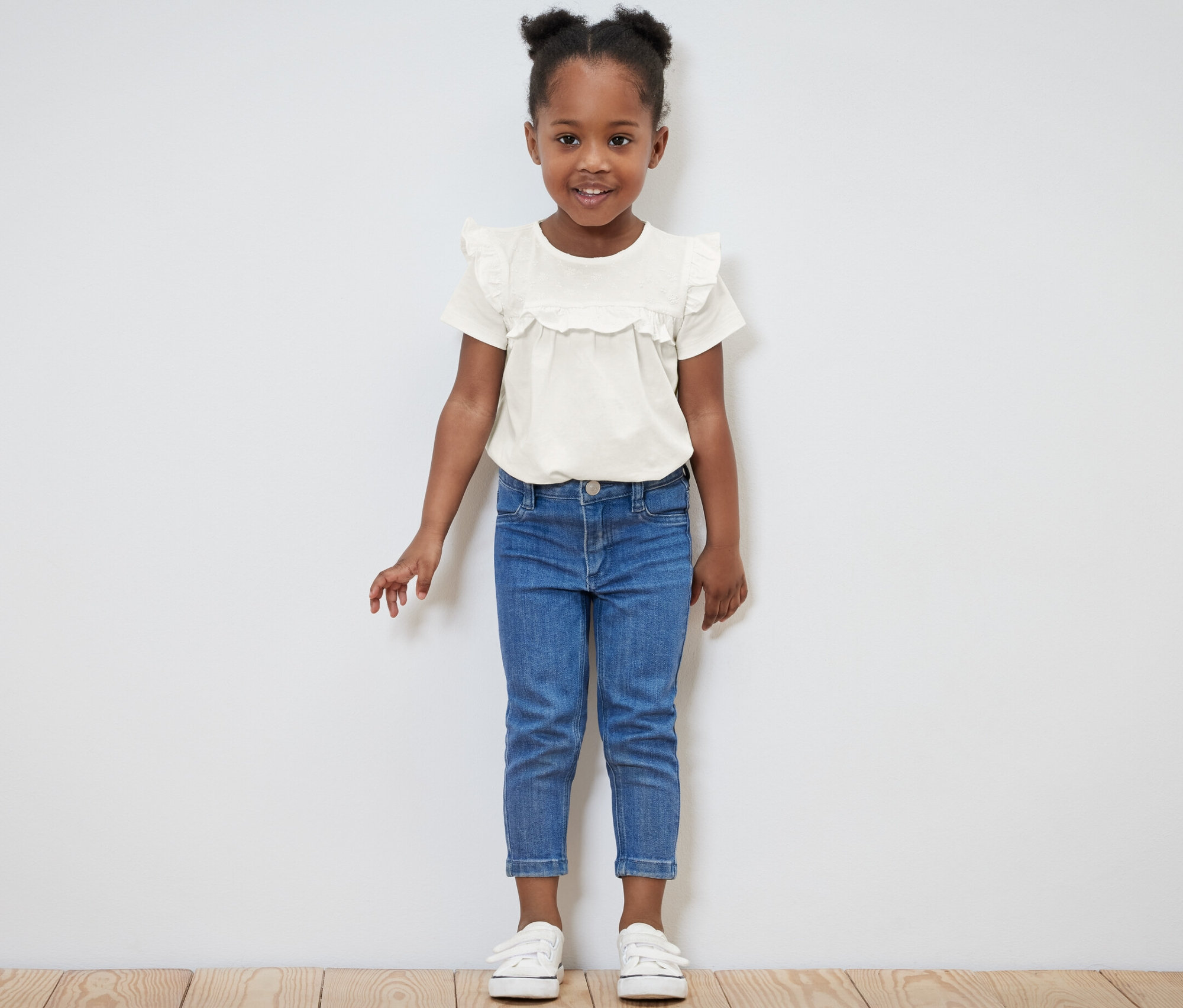 Lächelndes kleines Mädchen posiert in hellem Kinder-T-Shirt und blauen Jeans.