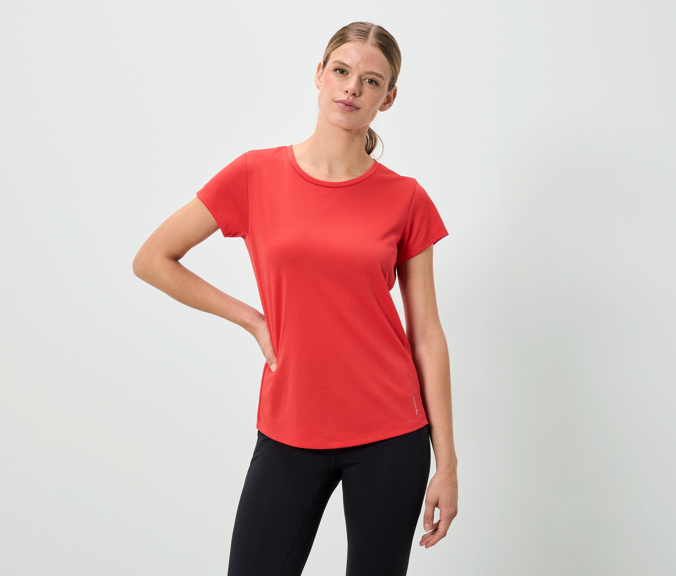 Eine Frau posiert in einem roten T-Shirt und schwarzen Leggings.