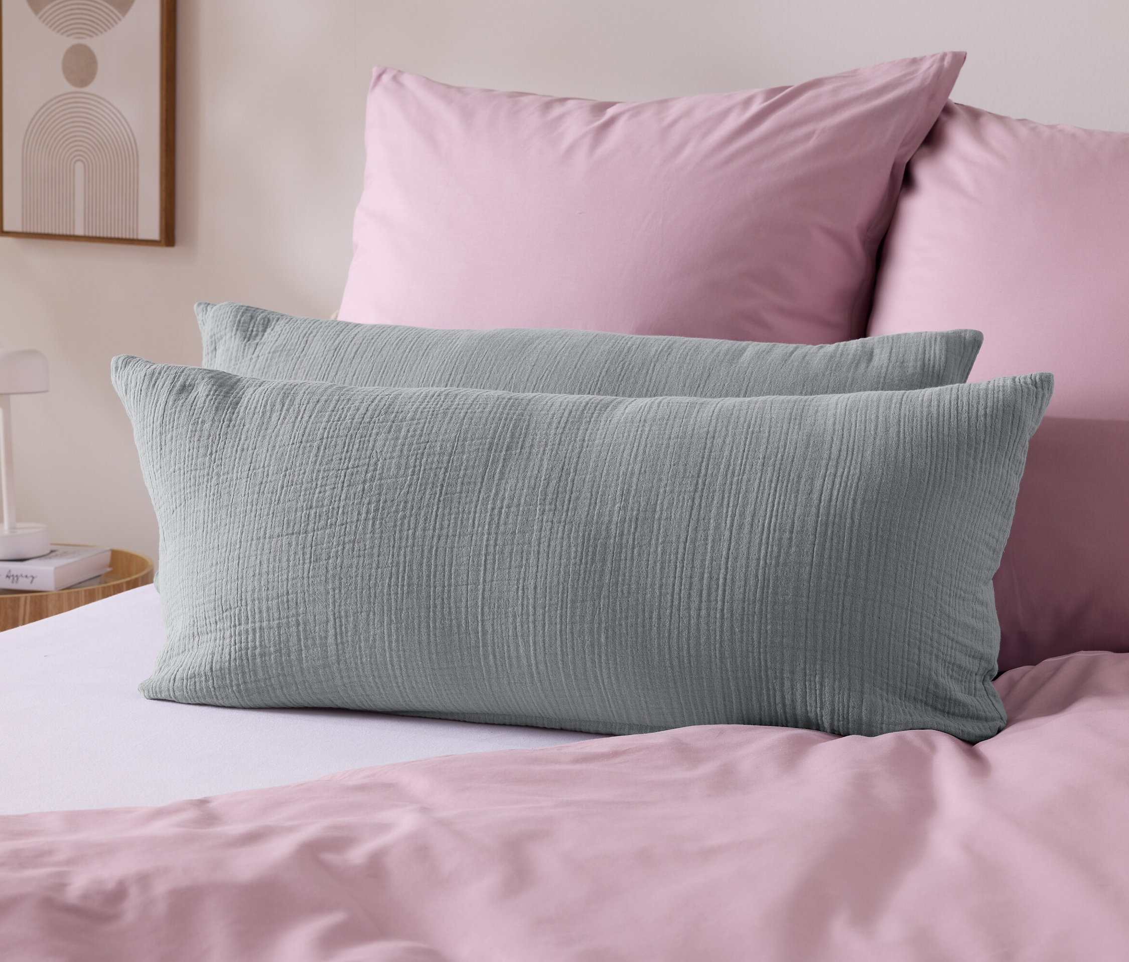 Zwei graue Kissen liegen auf einem weißen Bett mit rosa Bettwäsche.