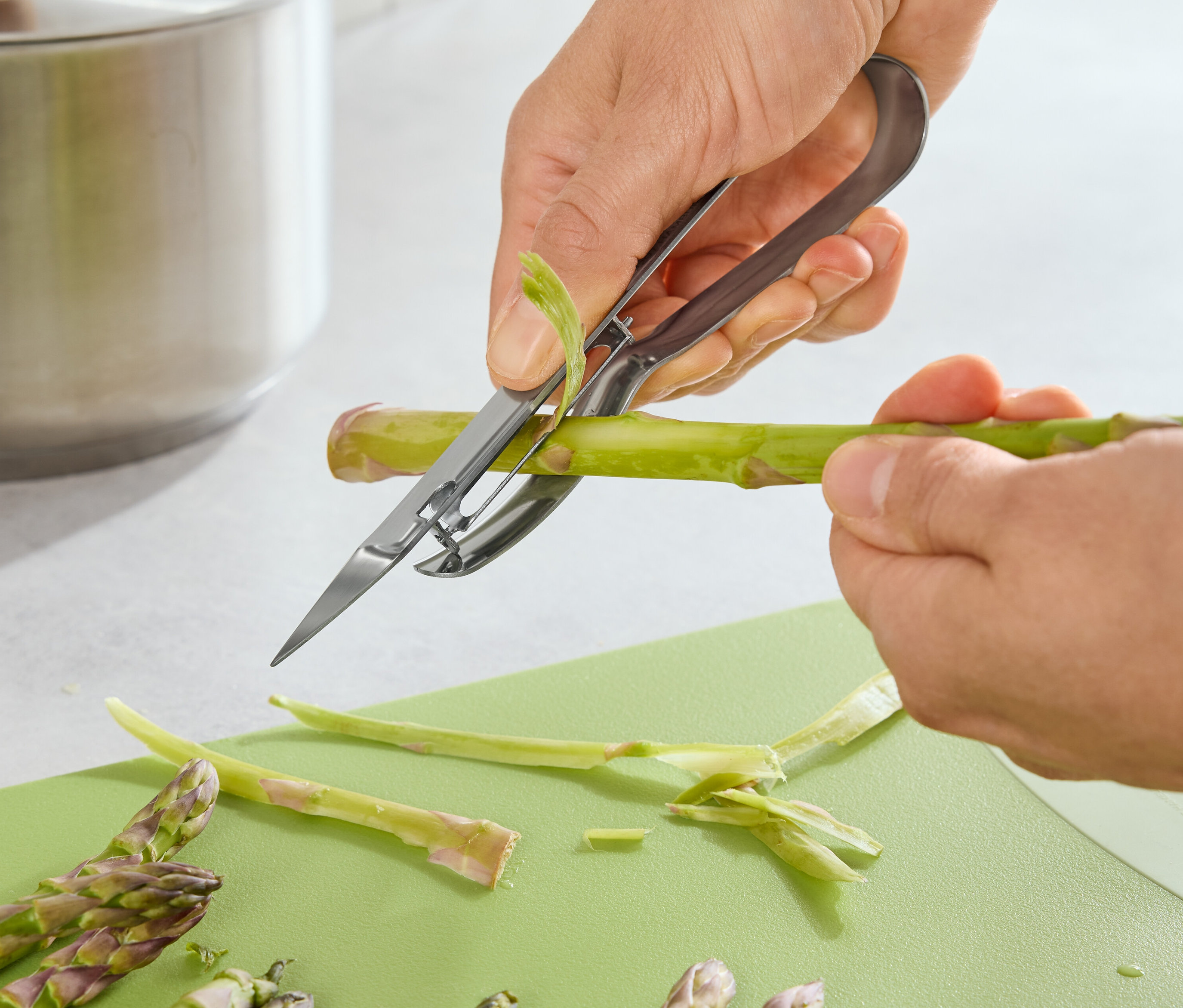 Eine Person schält Spargel mit einem Spargelschäler auf einem grünen Schneidebrett.