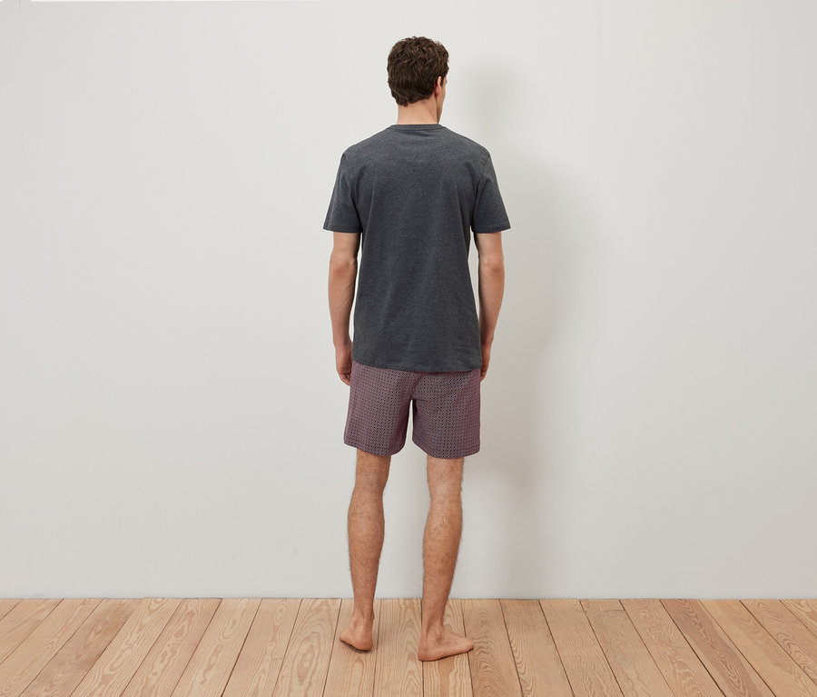 Mann von hinten trägt ein graues T-Shirt und karierte Shorts.