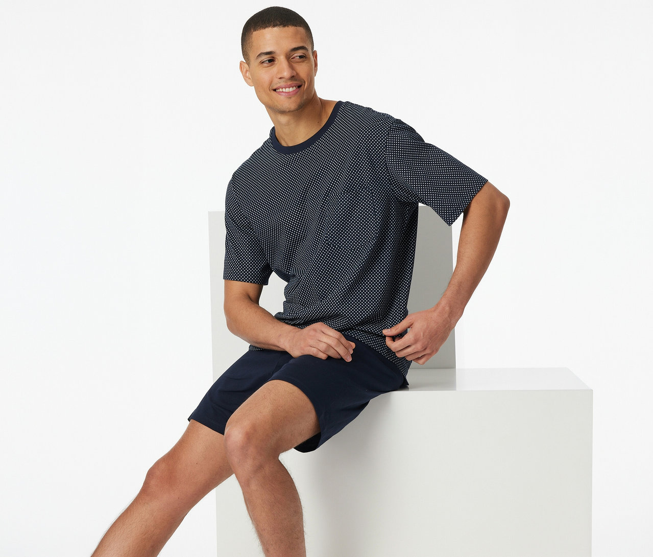 Mann sitzt im SCHIESSER Shorty-Pyjama-Set, bestehend aus marineblauen Shorts und einem kurzärmeligen, gepunkteten Oberteil.