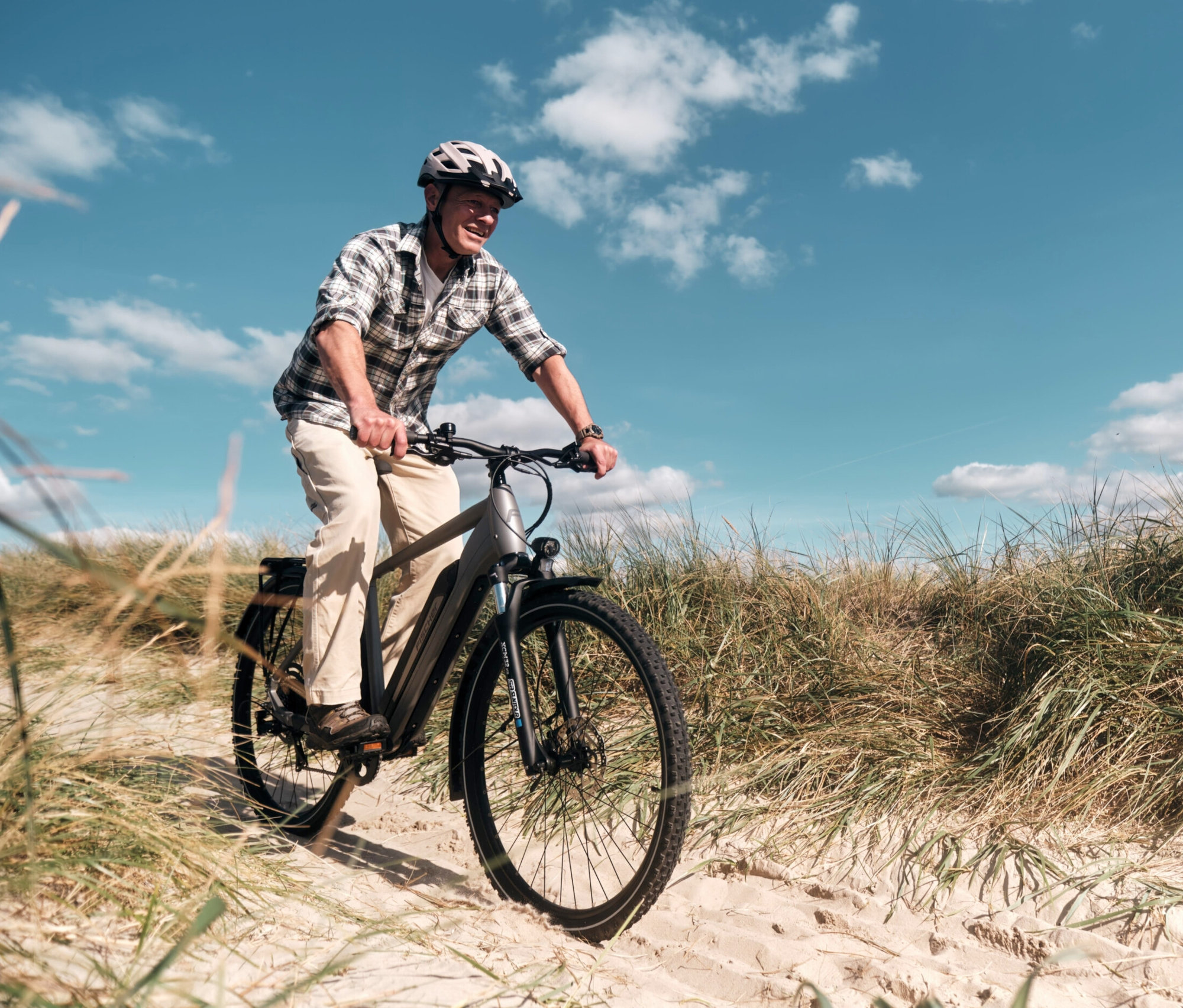 Mann fährt ein graues FISCHER Trekking-E-Bike TERRA 2.2 ACTIVE mit Diamant Rahmen auf sandigem Untergrund.