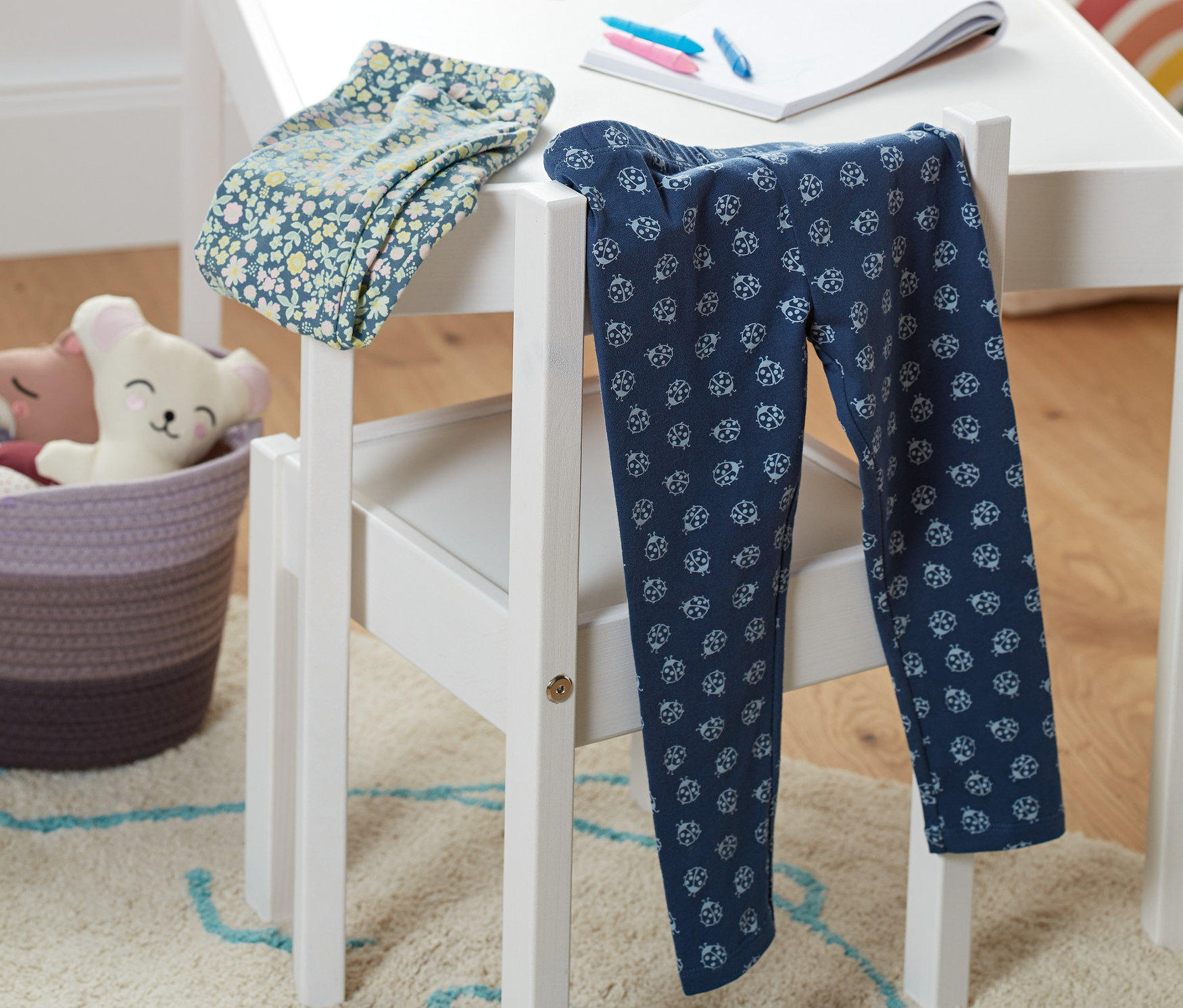 Zwei Leggings mit Alloverprint liegen auf einem weißen Kinderstuhl neben einem weißen Tisch.