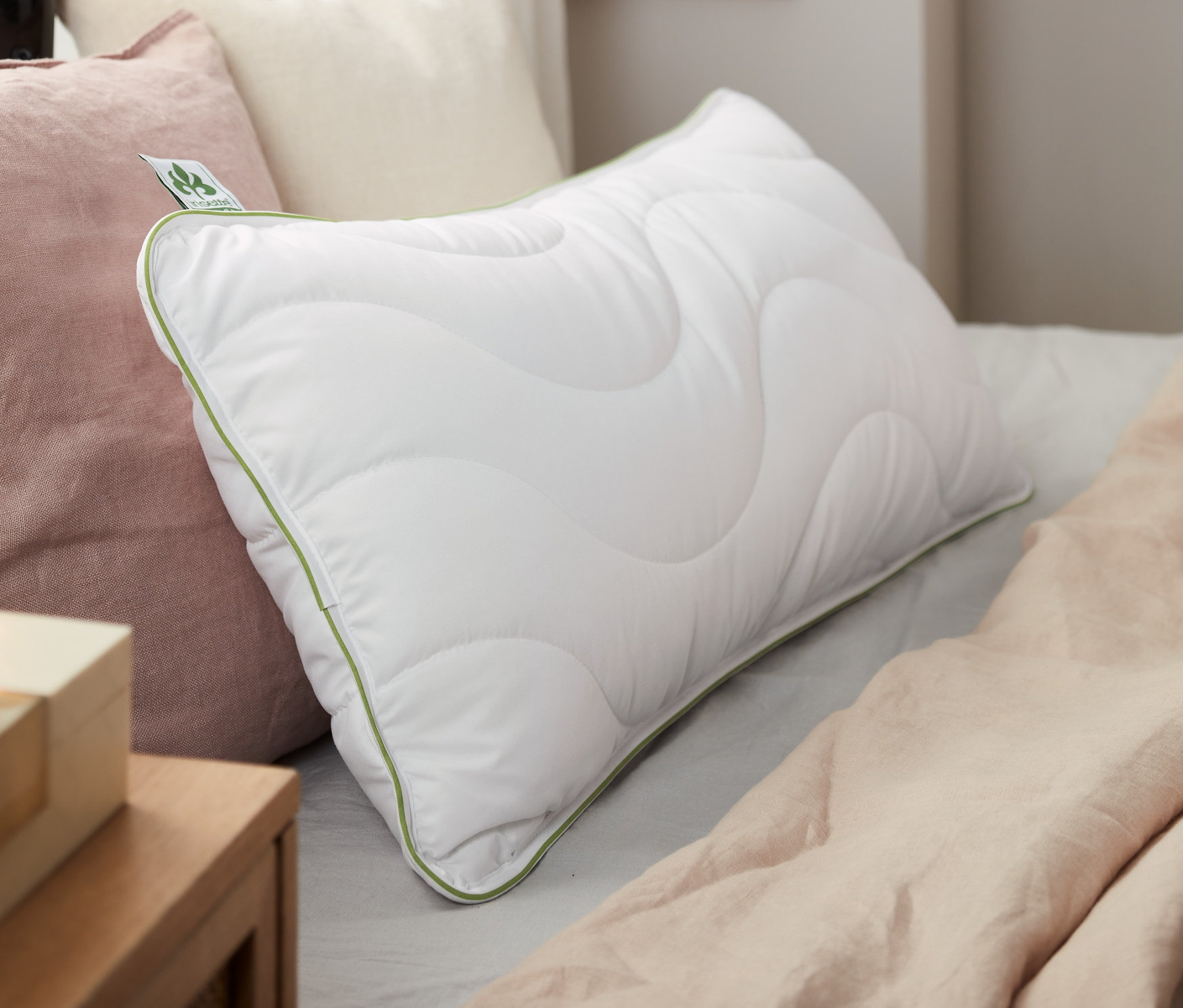 Auf einem Bett liegen zwei weiße irisette® greenline Kopfkissen, ca. 80 x 40 cm.