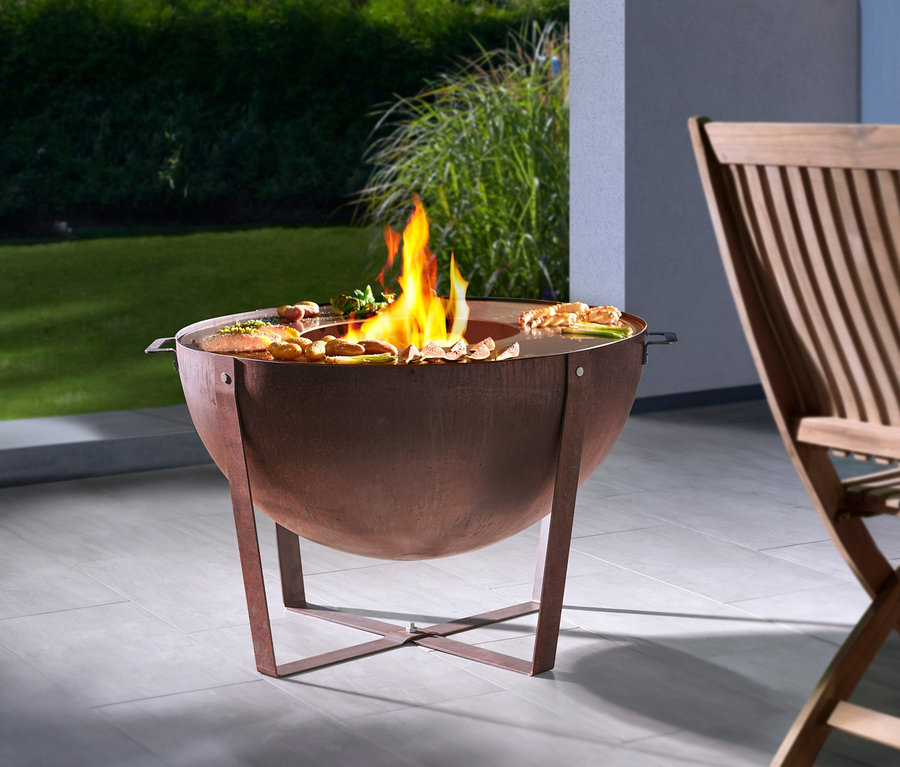 Buschbeck Plancha-Grill »Dakota« mit Flammen und Essen, Holzstuhl am Tisch.