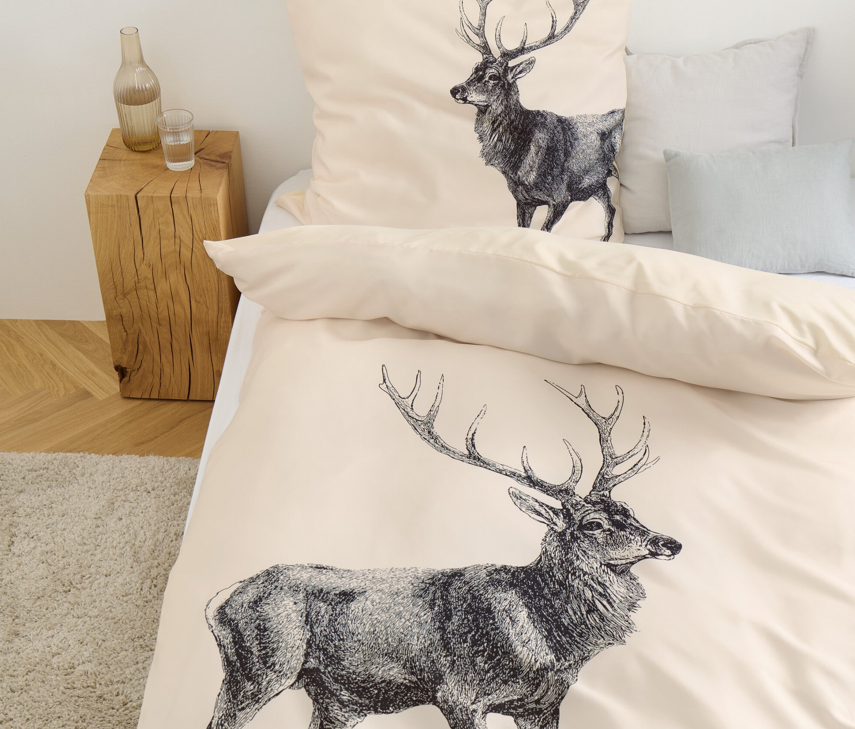 Beige Bettwäsche mit Hirschmuster liegt auf einem Bett.