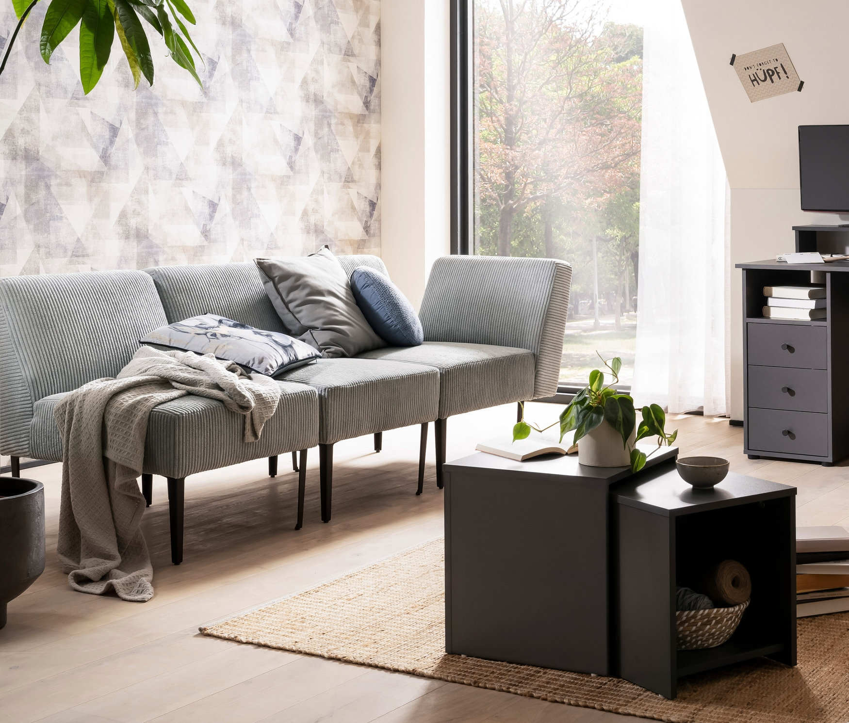 Wohnzimmer mit grauer DOMO collection Ecke »Karlsborg Leif55«, anthrazitfarbener Kommode »Smash«, Schreibtisch »Smash«, Schachteltisch »Smash« und Bildschirmtisch »Smash«.