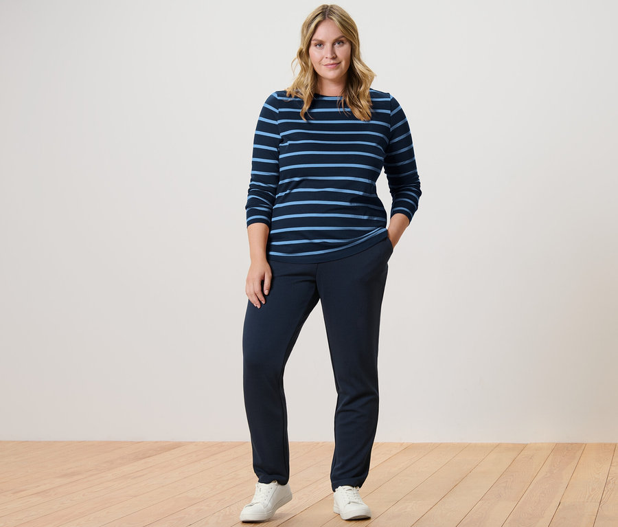 Frau steht in dunkelblauen Joggpants und einem gestreiften Langarmshirt.
