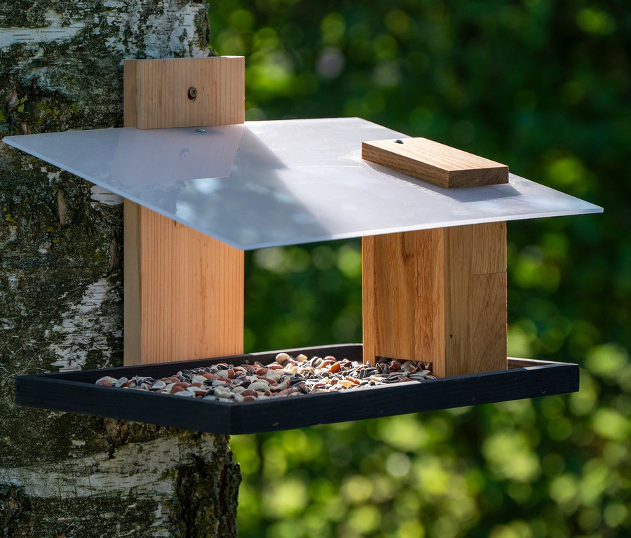 Ein Design-Vogelhaus »Futura I« ist an einem Baum befestigt. Das Vogelhaus ist mit Vogelfutter gefüllt.