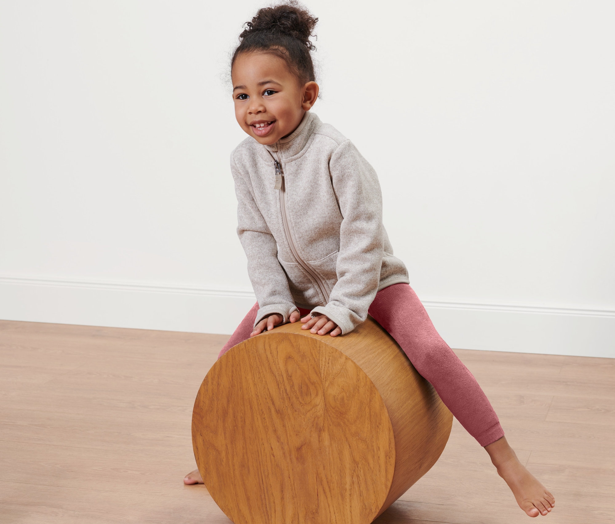 Mädchen sitzt auf einer Holzrolle und trägt rosa Thermoleggings.