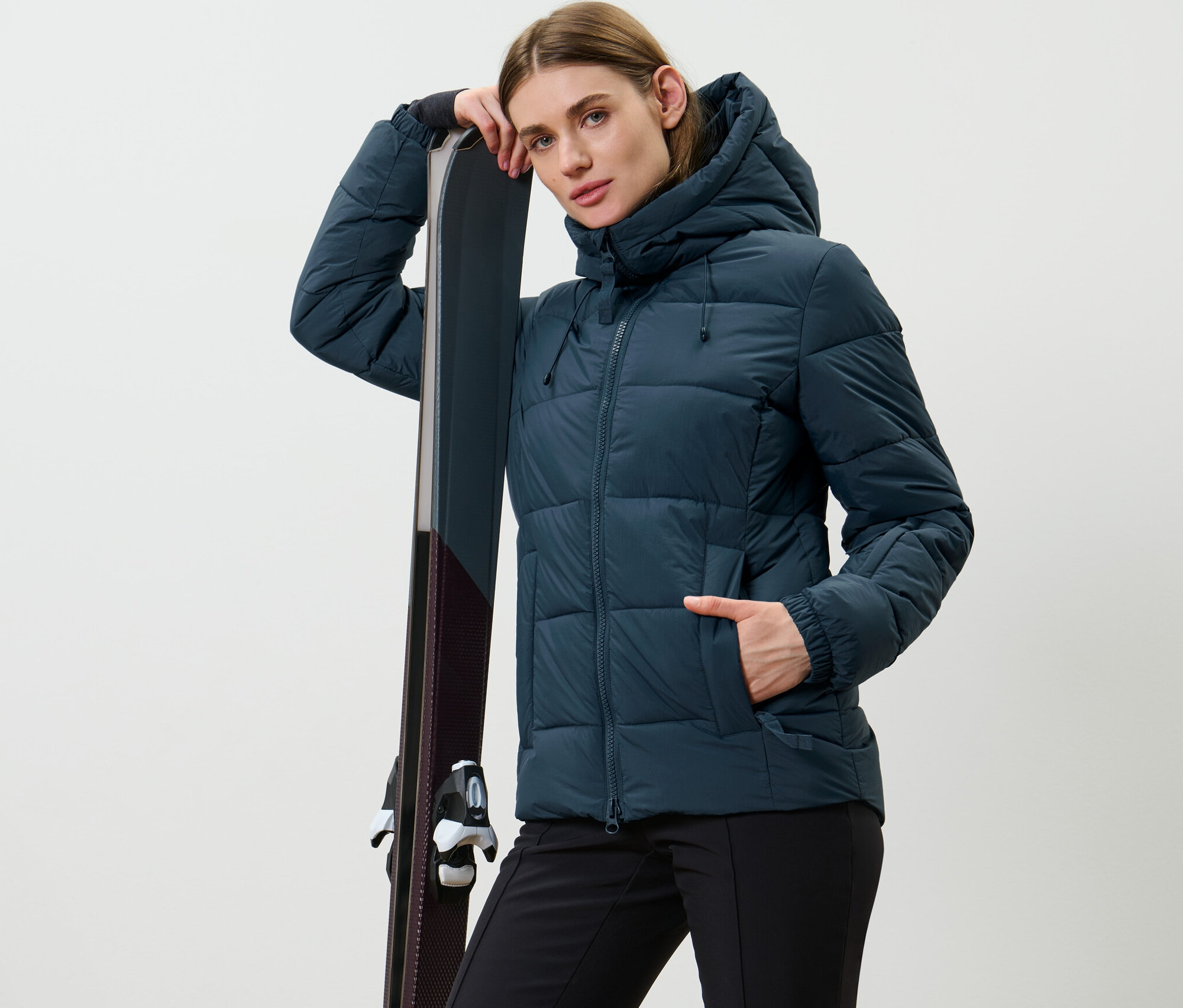 Frau posiert in dunkelblauer Ski-Steppjacke und lehnt sich an Ski an.