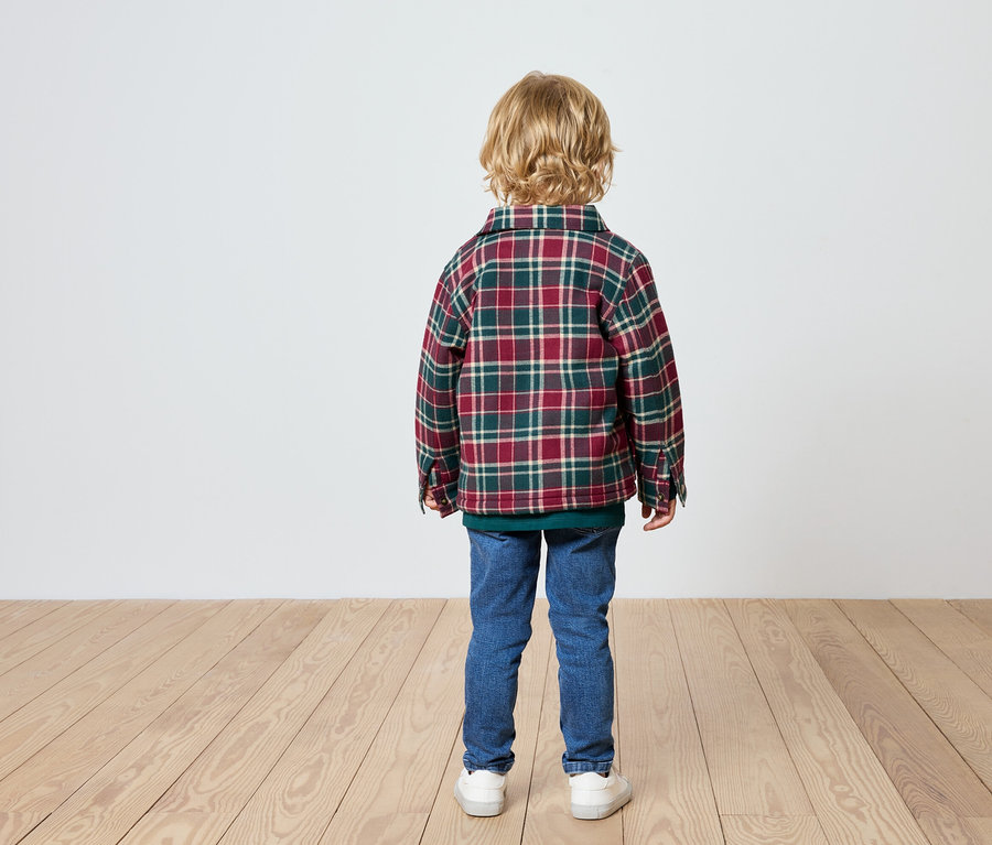 Junge steht mit dem Rücken zur Kamera, trägt ein kariertes Hemd, Jeans und Turnschuhe.