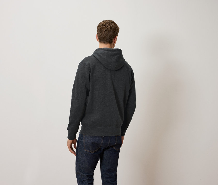 Ein Mann mit dem Rücken zur Kamera trägt einen dunkelgrauen Kapuzenpullover und Jeans.