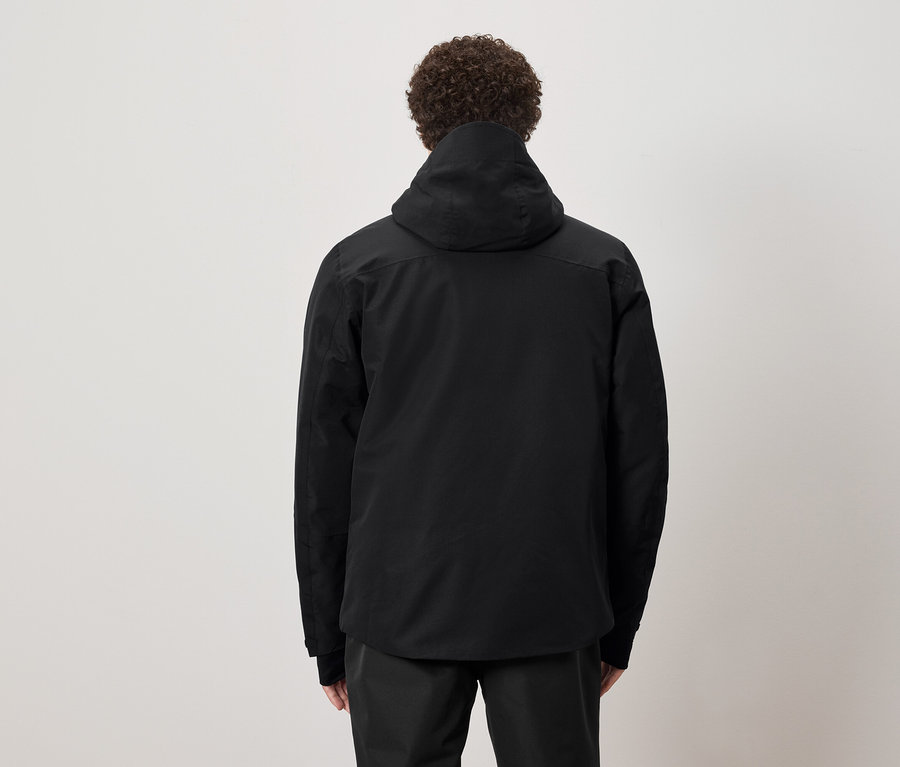 Mann mit lockigem Haar steht mit dem Rücken zum Betrachter und trägt eine schwarze Kapuzenjacke.